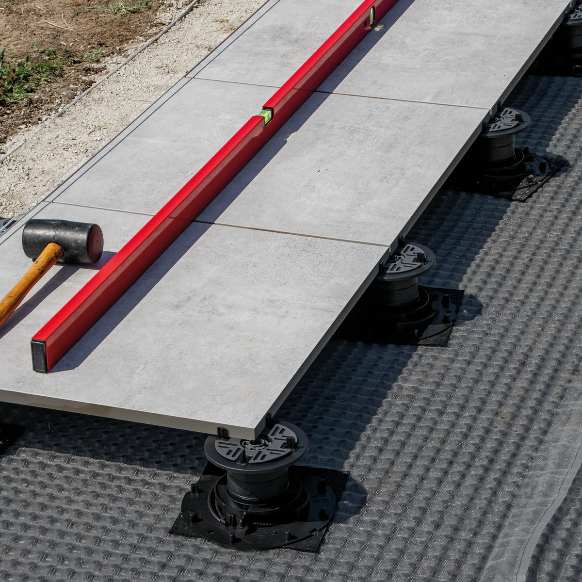 Ambience image of the pedestal supports on a terrace with anti-slip pads. The spirit level ensures that the tiles are installed on one level.
