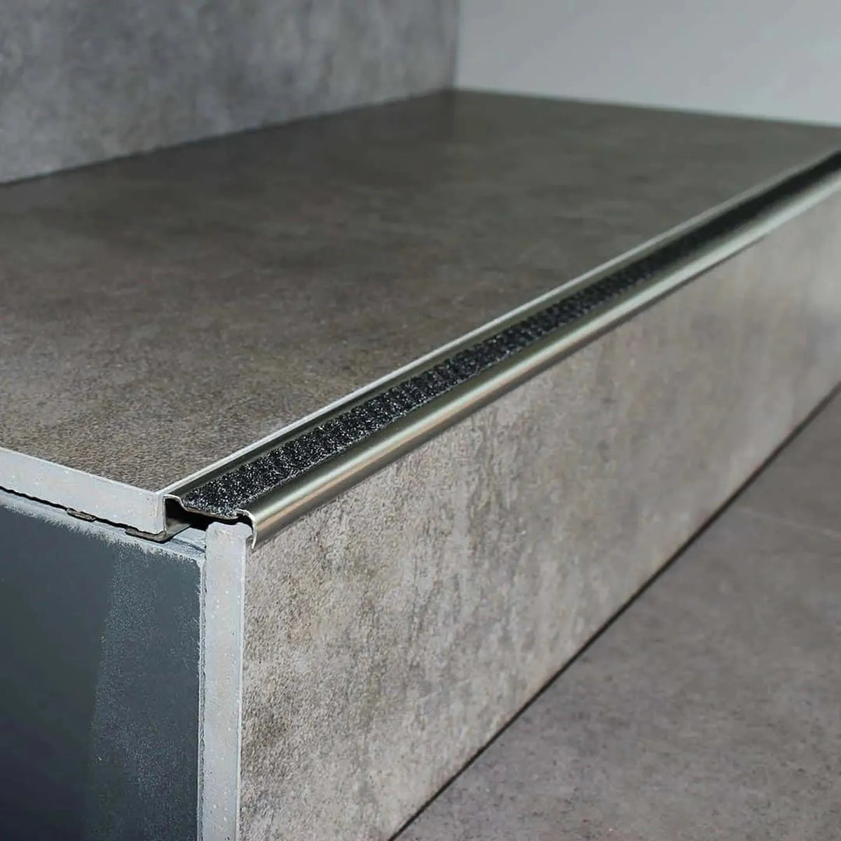 Profilé de nez de marche en aluminium antidérapant posé avec insert noir nuit sur une marche carrelée grise #A0001724
#A0002701