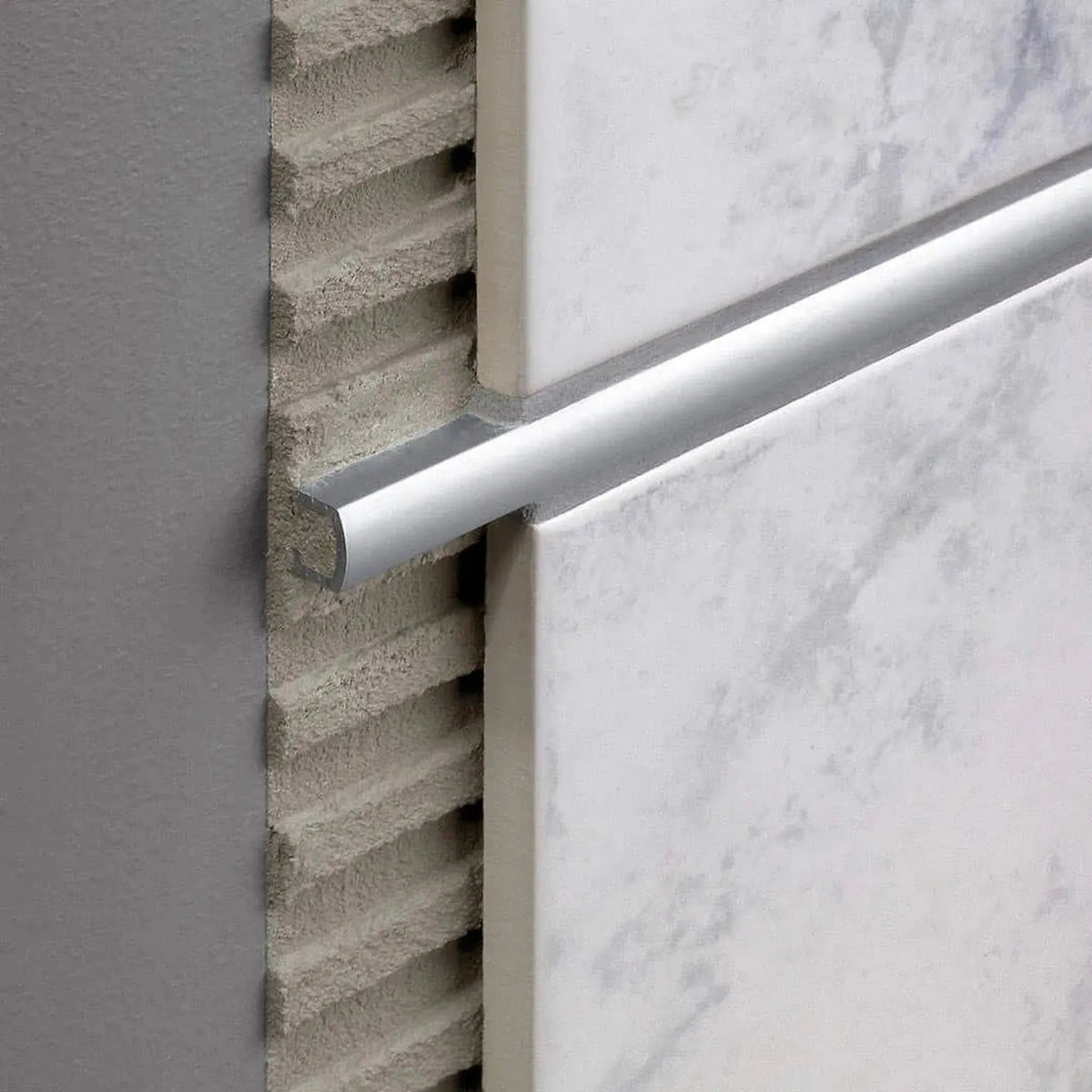 Verarbeitetes silbernes Dekorprofil mit weißen Fliesen. Ein Teil ist offen im Kleberbett #A0001641
#A0001645
#A0001646